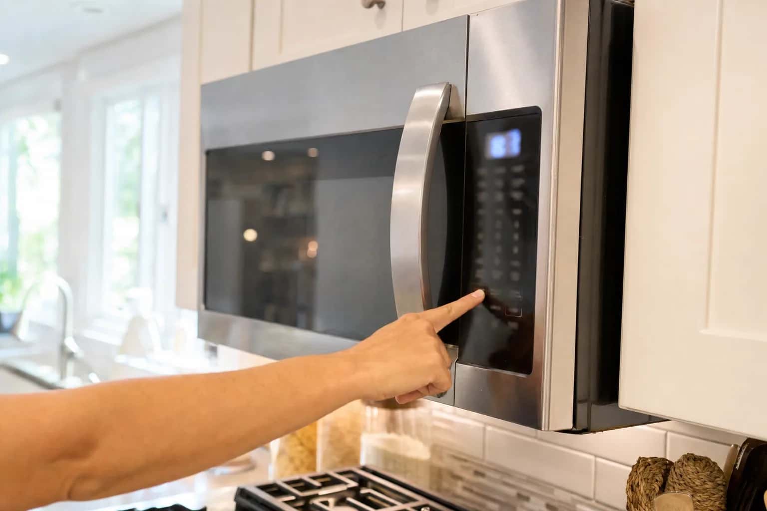 A finger pressing the keypad of a stainless over-the-range microwave