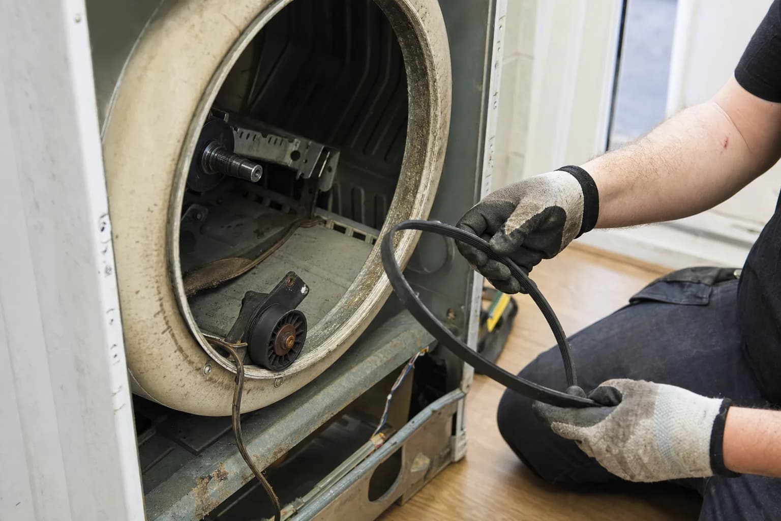 Clothes dryer with the drum removed, showing a worn drive belt and idler pulley being replaced