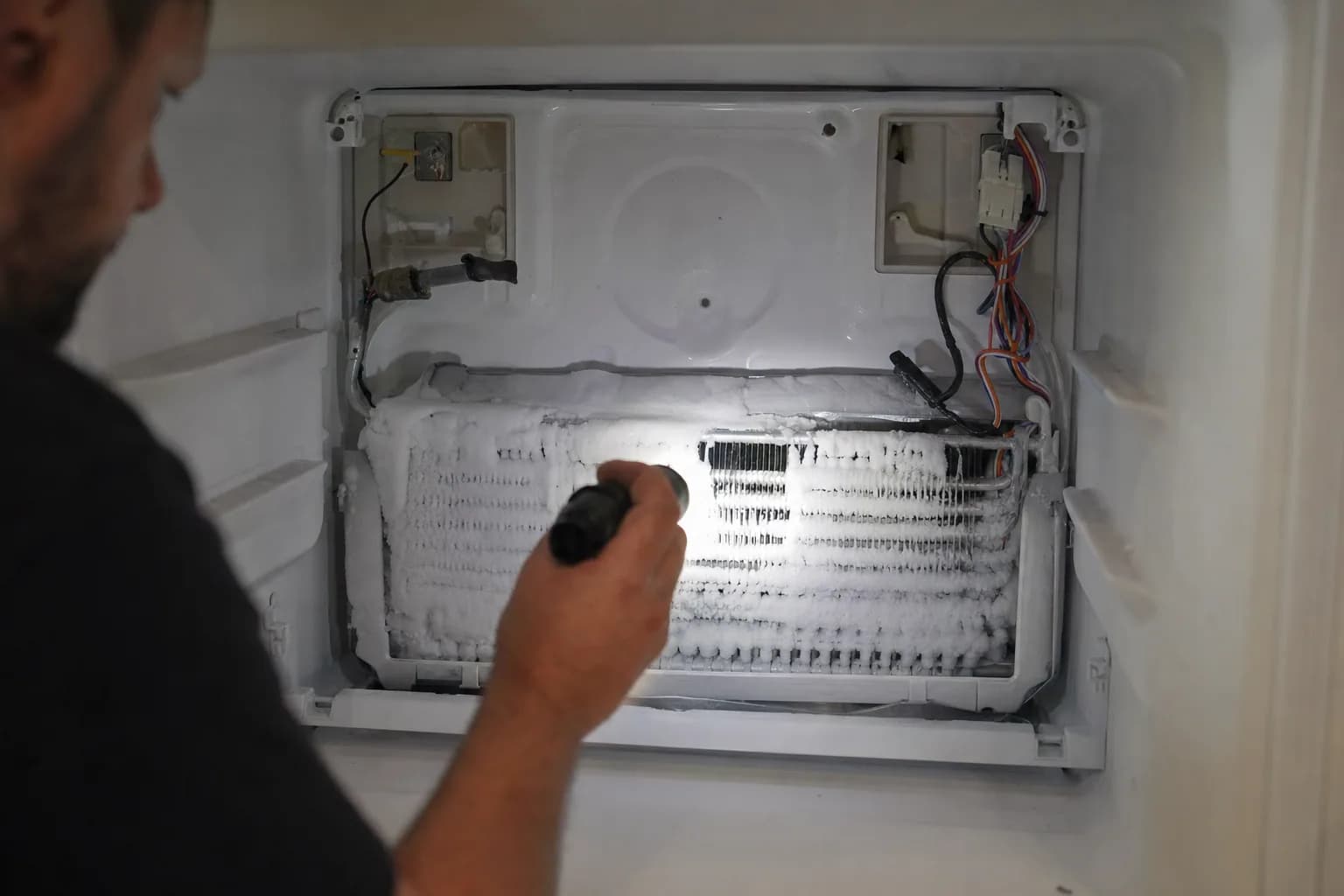 Freezer back panel removed to reveal a heavily frosted evaporator coil